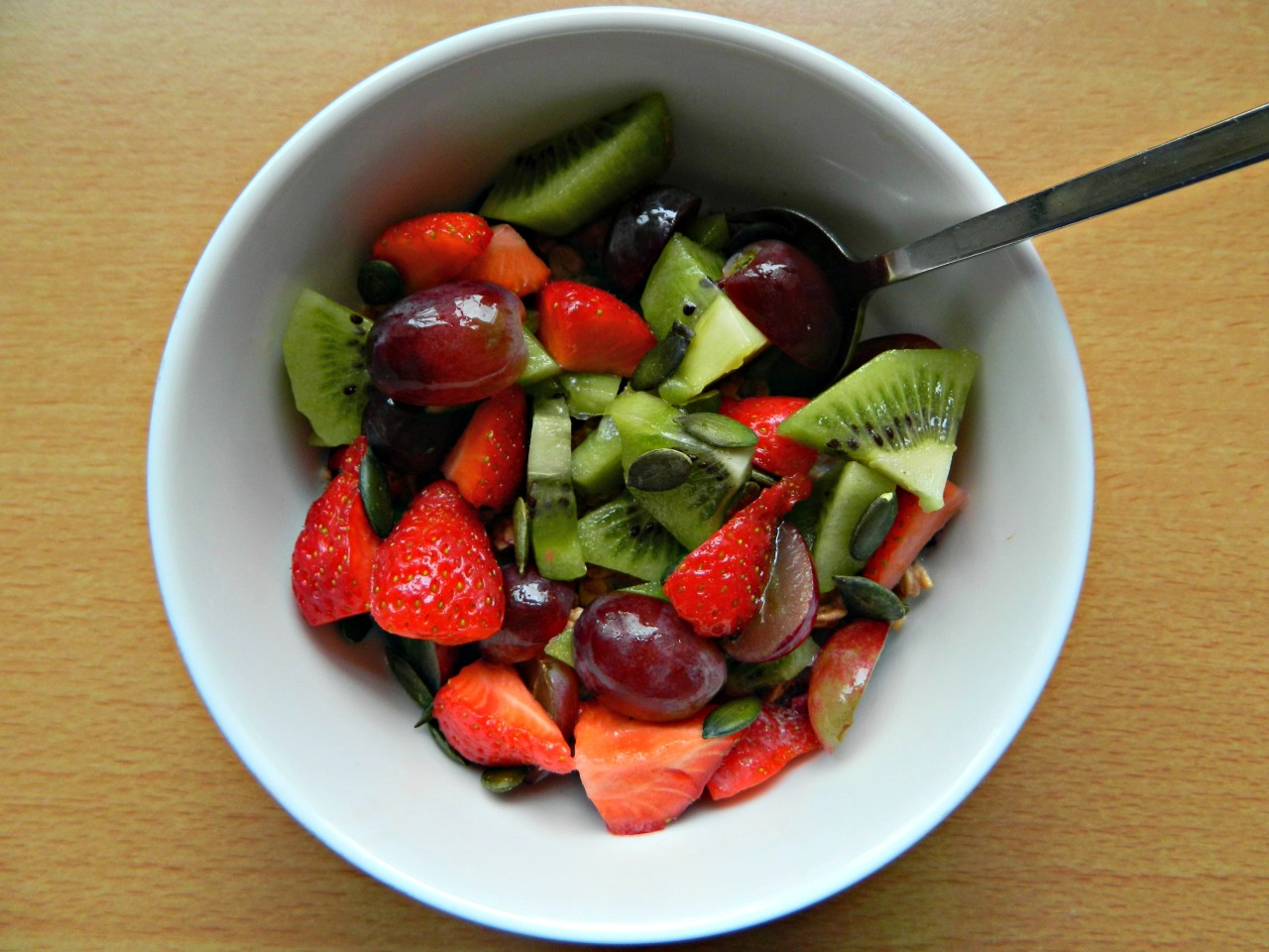 Super berry granola with cinnamon and almond milk, strawberries, red grapes, a kiwi and pumpkin seeds.