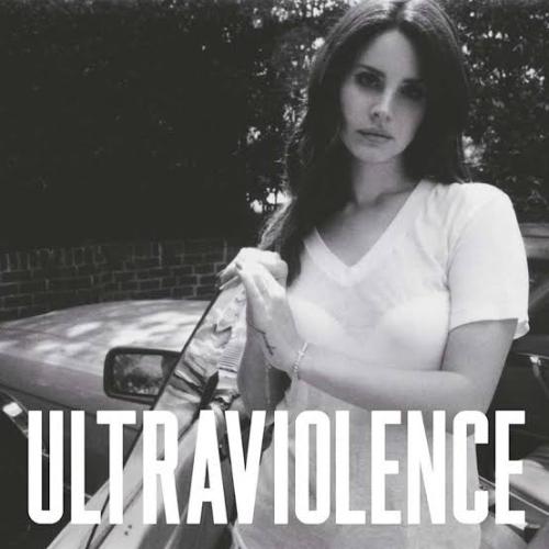 Lana Del Rey on black and white glances at our souls on a melancholic state. She is using a simple white t-shirt and is getting off a vintage car. Her dark hair falls over one shoulder and her back.