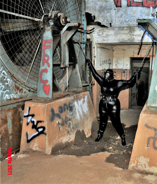 Polly chained in catsuit and gas mask.