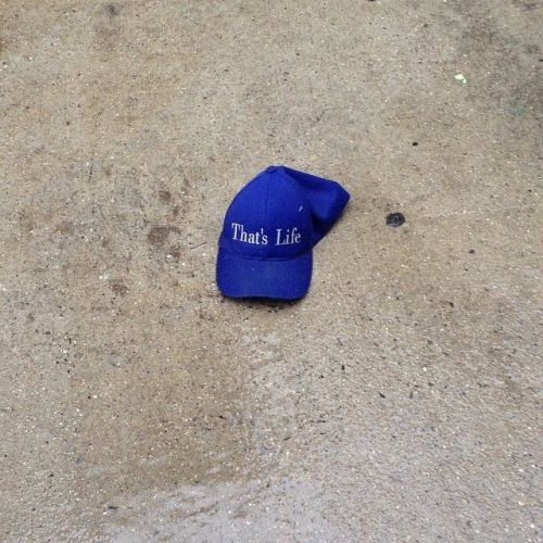 cookpot:[id: Photo of a blue hat lying crumpled up on a wet sidewalk. Text on the hat says, “T