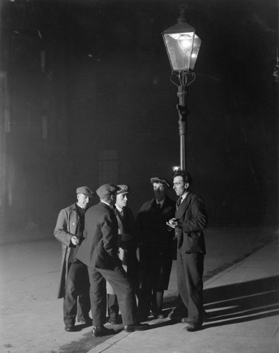 undr:Daily Herald Archive. A group of unemployed men gathered round a streetlight.