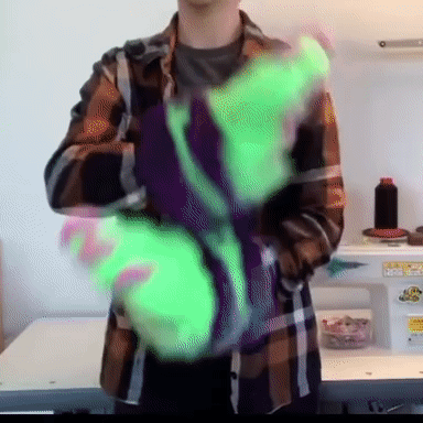 a gif of a white person in a plaid shirt wearing neon green fursuit paws and waving them left and right