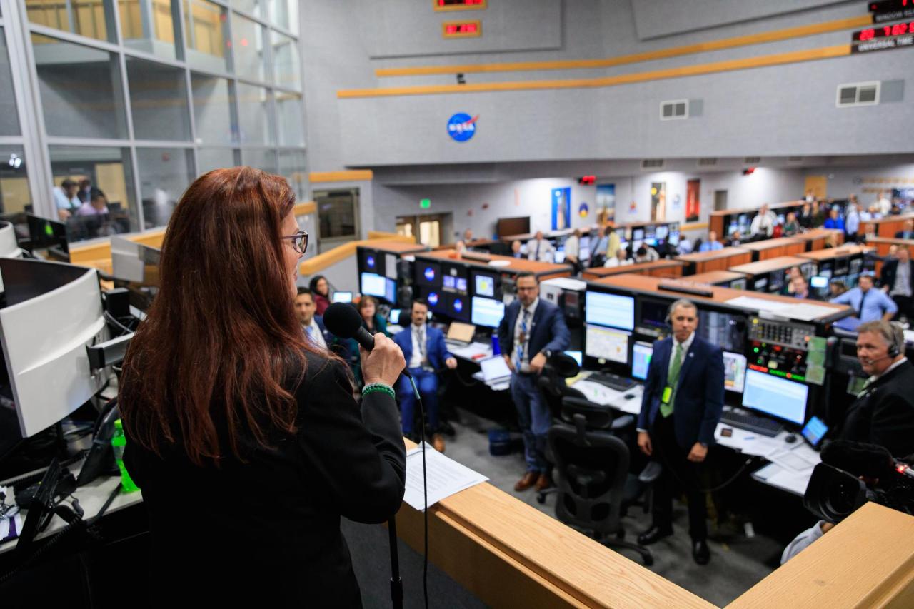 Artemis I Launch Director Charlie Blackwell-Thompson holds a microphone and addresses the launch team inside of the Launch Control Center. Members of the launch team are standing by their desks and looking up at where she is standing. Credit: NASA/Kim Shiflett