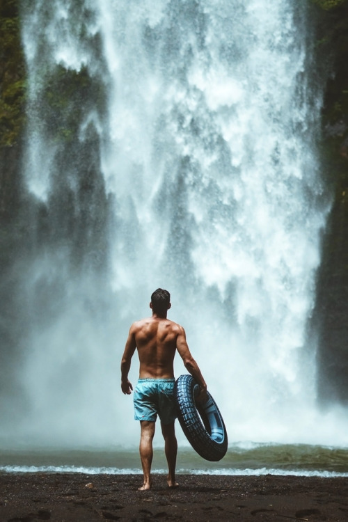 souhailbog:Man holding vehicle tire facing waterfalls By Oliver S