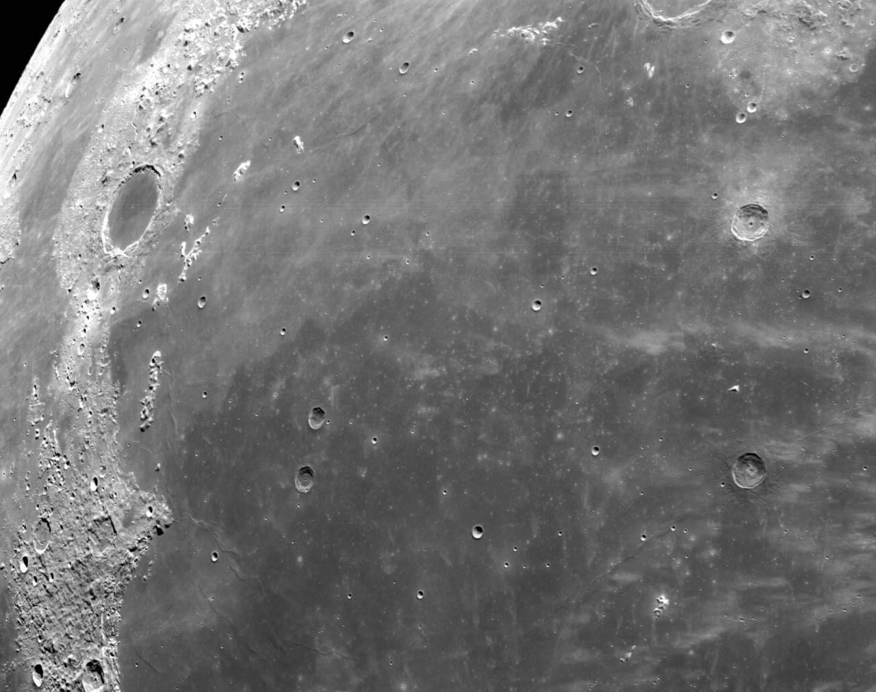 The lunar landscape varies from dark gray craters to white patches of plains. The blackness of space can be seen in the top left corner of the image. Credit: NASA