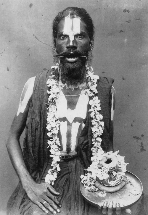 India, Sadhu with iron wire through cheek holds begging bowl with flowers