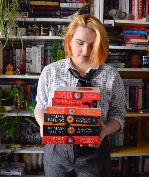 me, standing in front of my bookshelves, holding a stack of the bone season books in my hands
