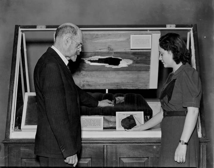 This meteorite crashed through the roof of the garage, the car roof, and the seat of the car before finally coming to a stop.
© The Field Museum, GEO79610.
Henry W. Nichols, Chief Curator of Geology, and Miss Caroline Ryder, examine the Benld...