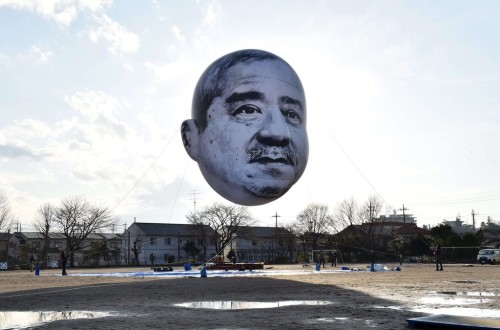 ofools:hollowedskin:shihlun:A giant helium balloon bearing the face of an ojisan (middle-aged man) a
