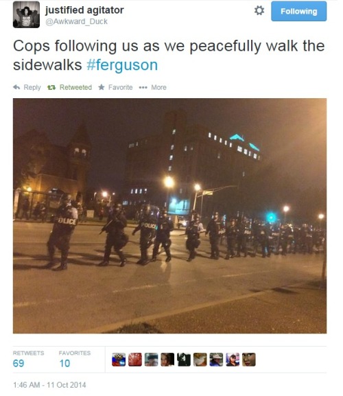 iwriteaboutfeminism:Police in riot gear follow peaceful protesters as they march down the sidewalk.E