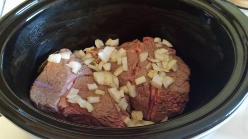 Chuck roast and chopped onions sitting in a black slow cooker.