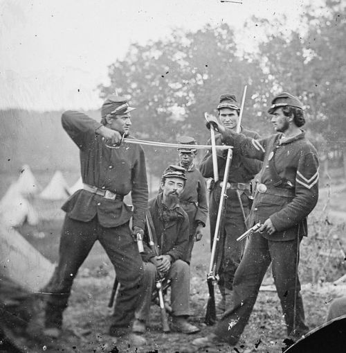 Two Union soldiers have a mock sword and gunfight in camp, 1863.