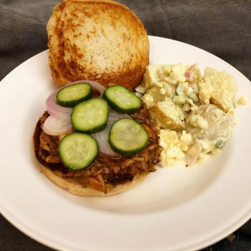 Pulled barbecue chicken sandwich with pickles and pickles onions and a side of southern potato salad