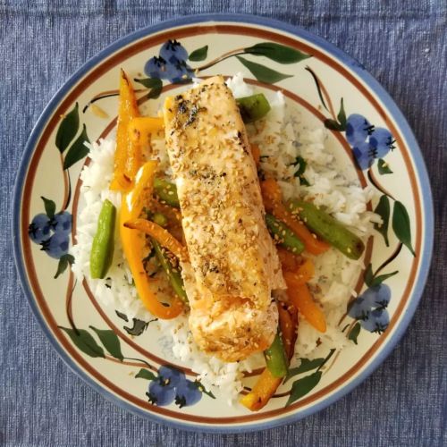 Grilled salmon topped with toasted sesame seeds on roasted orange peppers and snap peas over cilantr