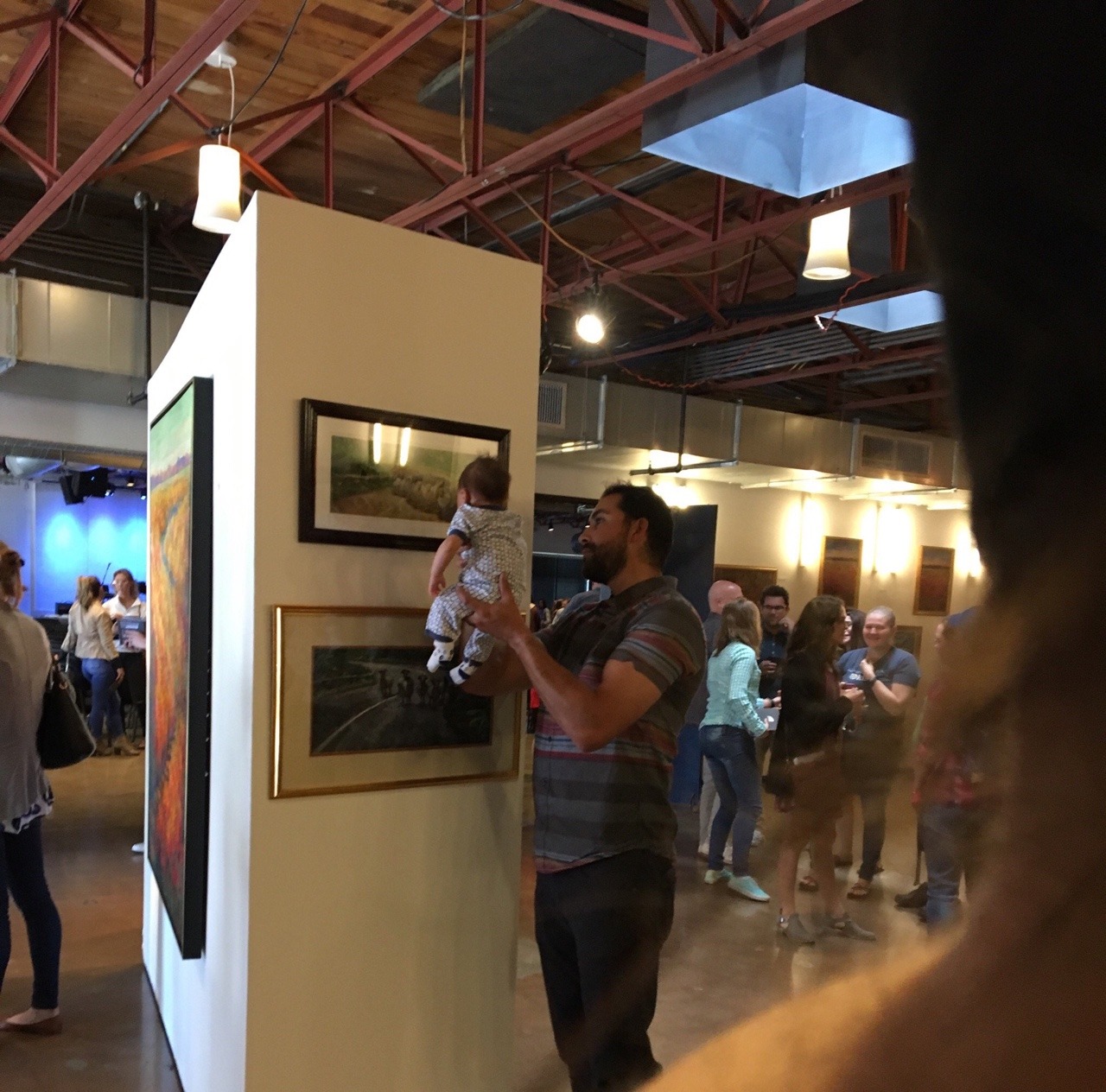 jafaaar:    A man holding his baby up to paintings and talking to him at an art gallery  