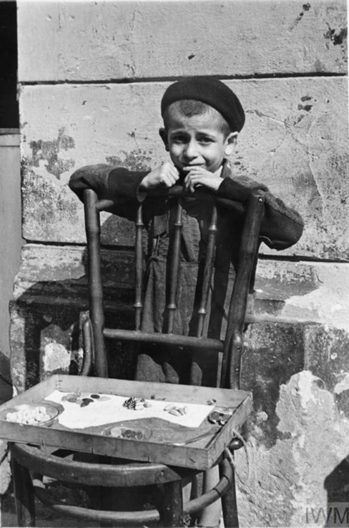 Warsaw Ghetto (Poland, 1941):A young boy selling a handful of sweets from a chair in the street.A yo