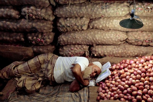 A Bangladeshi shopkeeper sleeps inside his onions shop at Karwanbazer wholesale market during a nati