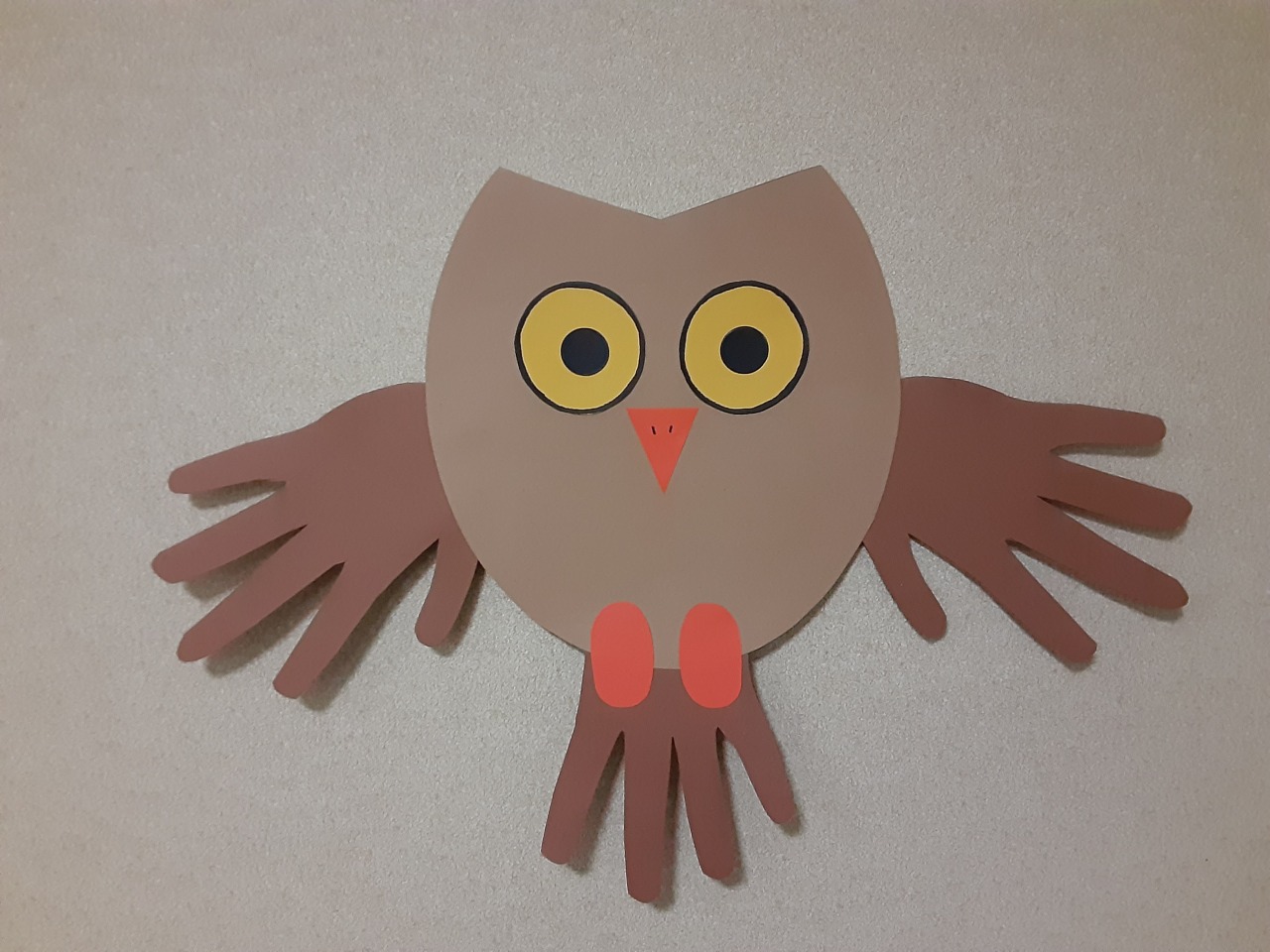 An owl cut out of construction paper with hand prints for wings and a tail