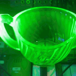 a person putting a geiger-müller tube into a teacup made from glowing green uranium glass.
