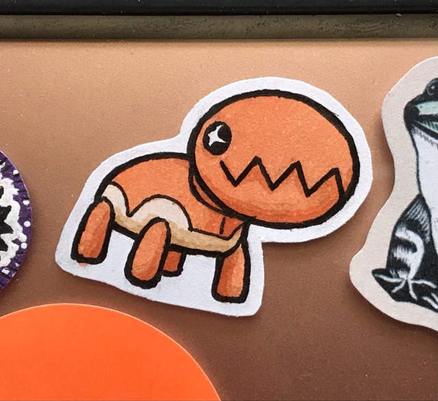 close up photo of one of the above trapinch stickers, now stuck amongst several other stickers to the back of a rose gold ipad