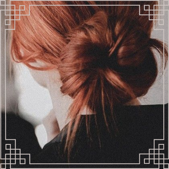 An image of a woman with red hair in a bun, bordered with a grey line interlocking at the four corners