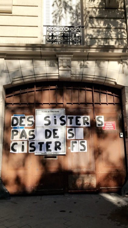 [Photo : white paper sheets stuck to a gate in Paris, France. They form the slogan “Sisters no