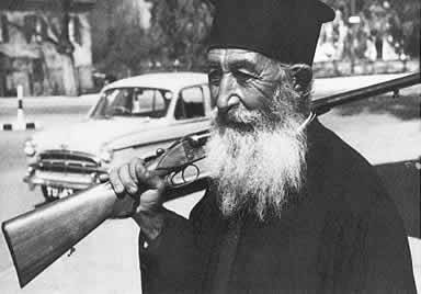 A Greek orthodox priest shoulders his shotgun in the service of the Greek ‘Home Guard’ i