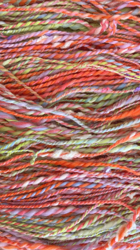 Colorfun handspun yarn, zoomed in to show chunky and very textured strands. The yarn has gold glitter fiber in it and is vibrant orange, green, and purple.