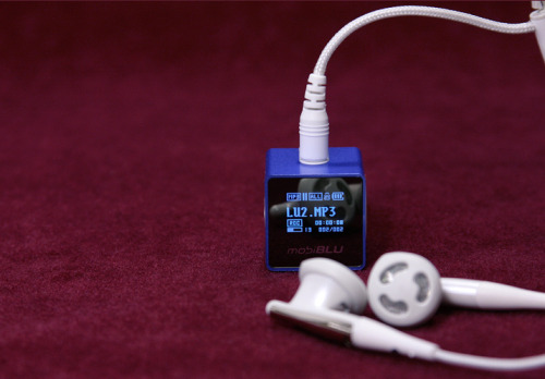 Red Background. Image of MobiBlue MobiBLU DAH-1500i mp3 in the color blue. Blue digital text against the mp3's LSD screen. There are white headphones plugged into the device coming into frame.