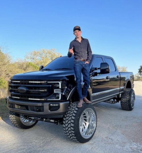 In The Dim Light Of The Evening, A Lifted Ford Truck Rumbled Down The Highway, The Wide, Tall Wheels