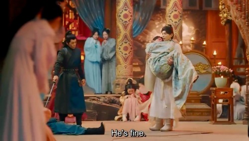 Screenshot of a scene from the Chinese-Taiwanese drama "Meet You at the Blossom" of Zheng Huaien carrying an unconscious Jin Xiaobao in his arms bridal style as he walks through a brothel. People around him are cowering in fear as he walks passed. English subtitles read, "He's fine".