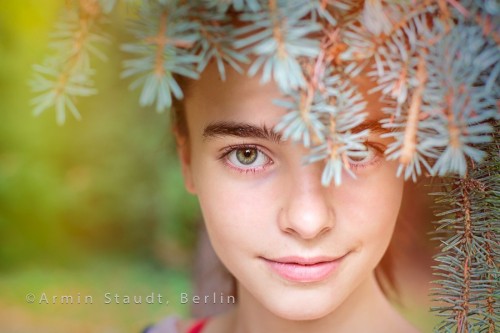 portrait of a smiling girl looking through blurred fir needles
