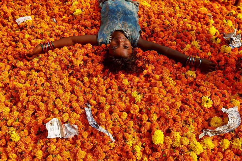 fotojournalismus: A girl rests on a pile of discarded flowers outside a market, a
