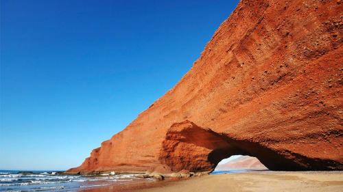 Find shade under a beach canopy carved by Mother Nature herself. Sea-worn, red-rock archways welcome