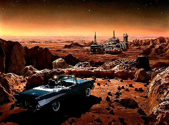 GIF 6: wide shot of a red desert planet's surface. in the foreground a blue convertible with the roof down is parked. two people are sitting inside it. the are overlooking a vast valley. in the valley, in the right center of the frame, is a group of buildings, some towers, some with slightly dome shaped roofs. the sky is coloured a warm orange and stars are blinking.