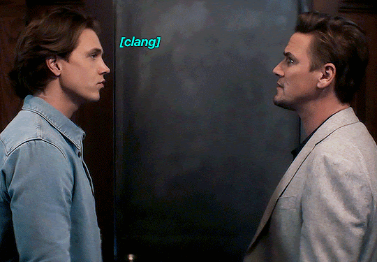 GIF FROM EPISODE 3X08 OF NANCY DREW. ACE AND RYAN ARE STANDING IN THE ARCHIVE ROOM OF THE HISTORICAL SOCIETY, IN FRONT OF THE CLOSED DOOR. THE TEXT ON THE GIF INDICATES THAT THERE'S A SERIES OF CLANGS, AS RYAN LOOKS AROUND AND ACE JUST STARES AT HIM.