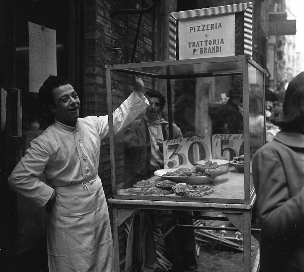 historicaltimes:  A shop boy selling pizza at a street market in Naples, Italy, in