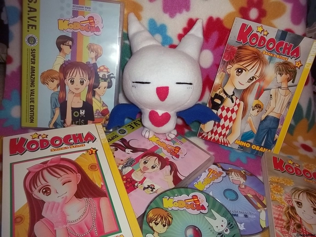 A handmade plush of Babbit from the anime/manga Kodocha, pictured alongside various DVDs and books of the series. He's sewn to have a big smile!