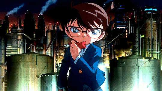 A GIF from the 25th opening sequence for Detective Conan/Case Closed, set to the song "Revive" by Mai Kuraki. It's nighttime, and Conan walks very seriously and deliberately. As he walks, he removes his bow tie and throws it to the ground, and then he does the same for his glasses, and finally, he shoots the tranquilizer dart on his watch forward. The screen becomes white in a flash of light.