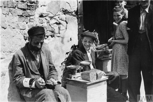 Warsaw Ghetto (Poland, 1941):An elderly Jewish woman selling her scarce possessions in the street.A 