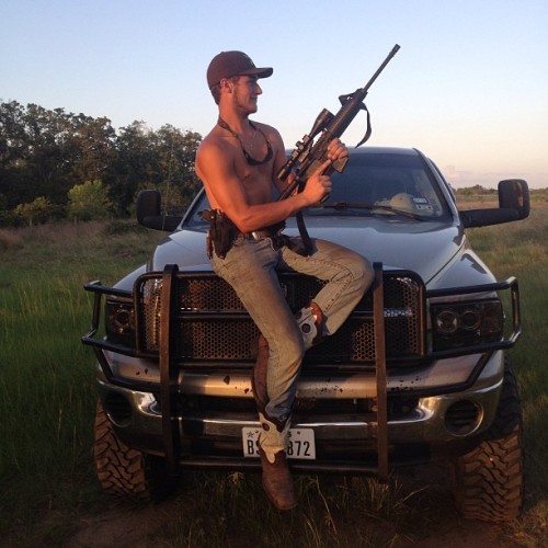 Shirtless Southern Boy sitting on the hood of his pick-up truck holding his gun.