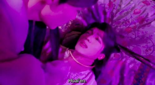 Screenshot of a scene from the Chinese-Taiwanese drama "Meet You at the Blossom" of Jin Xiaobao lying in bed being strangled by Zheng Huaien, who is leaning over him. Xiaobao's mouth is slightly parted as he gasps for air. The lighting is shades of pink and purple adding to the hazy intoxicated vibe of the scene. English subtitles read, "Huai'en."