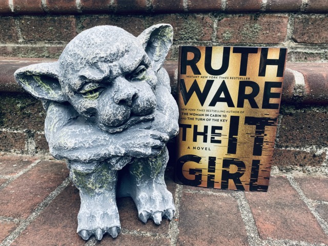 Pictured is THE IT GIRL (black letters on gold background) on stone steps, sitting beside a stone gargoyle. Photo by AHS.