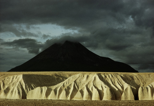 Sheer 100-foot cliffs of eroded ash rise before Mount Katolinat in Alaska.Photograph by Winfield Par