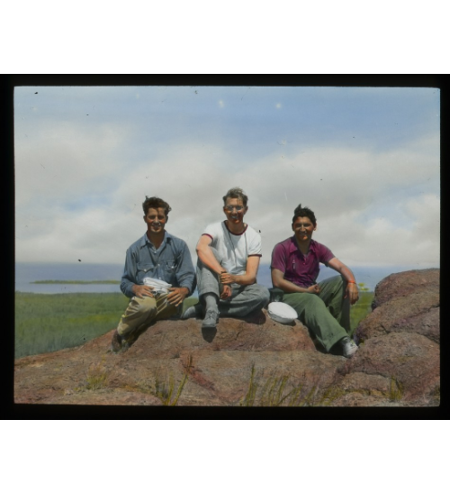 Hand tinted Lantern slide showing an image of three men sitting on rocks.Isle Royale, MI  1930