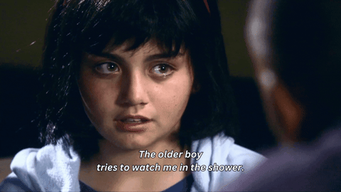 Ellie hesitates before speaking, a tear rolling down her cheek. White subtitles read: "The older boy tries to watch me in the shower."