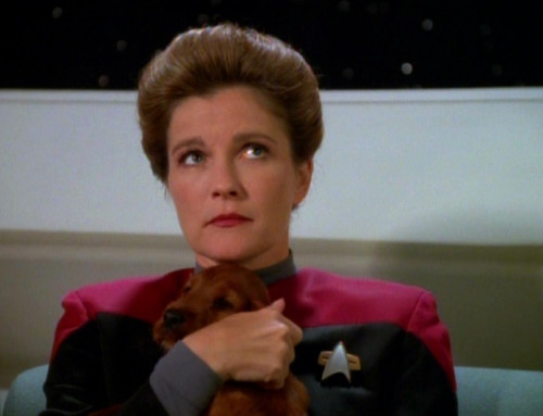 startrekhugs:[Image: Captain Janeway cuddles a puppy, looking annoyed. From The Q and the Gray. Imag