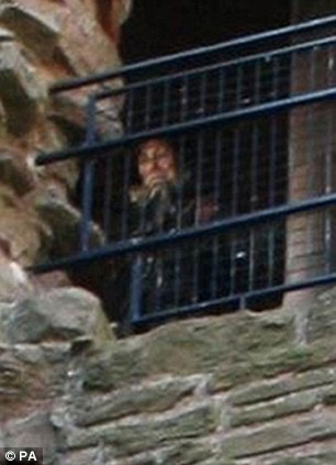 In The Ruins Of A Scottish Castle An Elderly Woman Peers Down From A Window. She Seems To Be Wearing