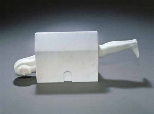 Image of a sculpture called Femme Maison by Louise Bourgeois. A minimalist white block that looks like a house sits on the ground. It is a rectangle with a triangle roof and one rounded indentation like a door in the center. A minimalistic woman's head sticks out of the left side, turned slightly from the ground to look at the viewer. Whether her eyes are opened or closed is impossible to tell. Her calves stick out of the right side of the house at a higher point so that her body must be positioned in a straight slope with her head pointing further towards the ground.