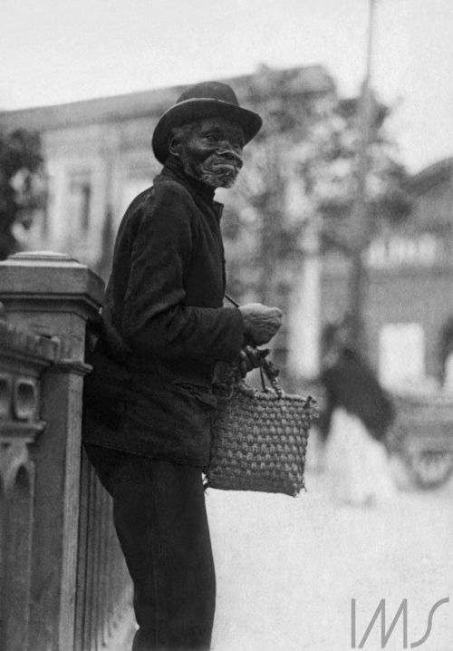 1) Retrato de homem idoso recostado em grade metálica da rua São João (circa 19